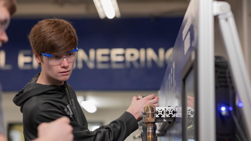 Student working on a copper pipe in with an engineering sign in the background.